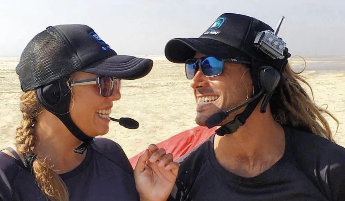 2 people wearing BbTalkin headsets, smiling at each other on the beach