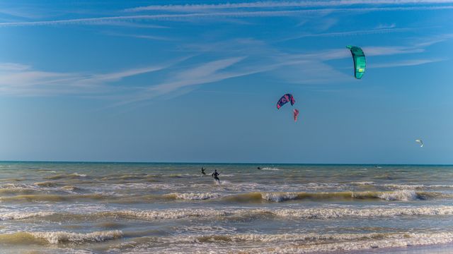 kitesurfers on the beach infront of a blue sky and rough see