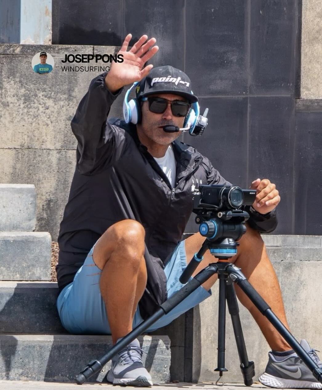 Josep Pons sitting on a step wearing a BbTalkin headset and using a video recorder, waving to the camers