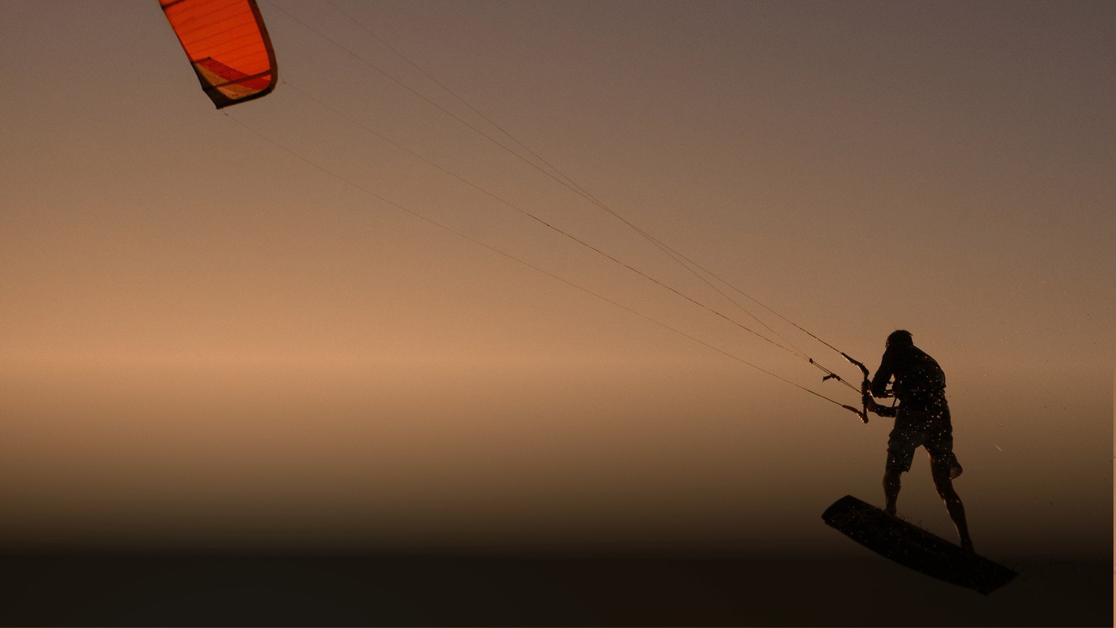 Person kite surfing at sunset with a kite in the air