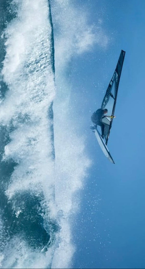 Josep Pons Surfing in the air above a large wave with a clear blue sky.