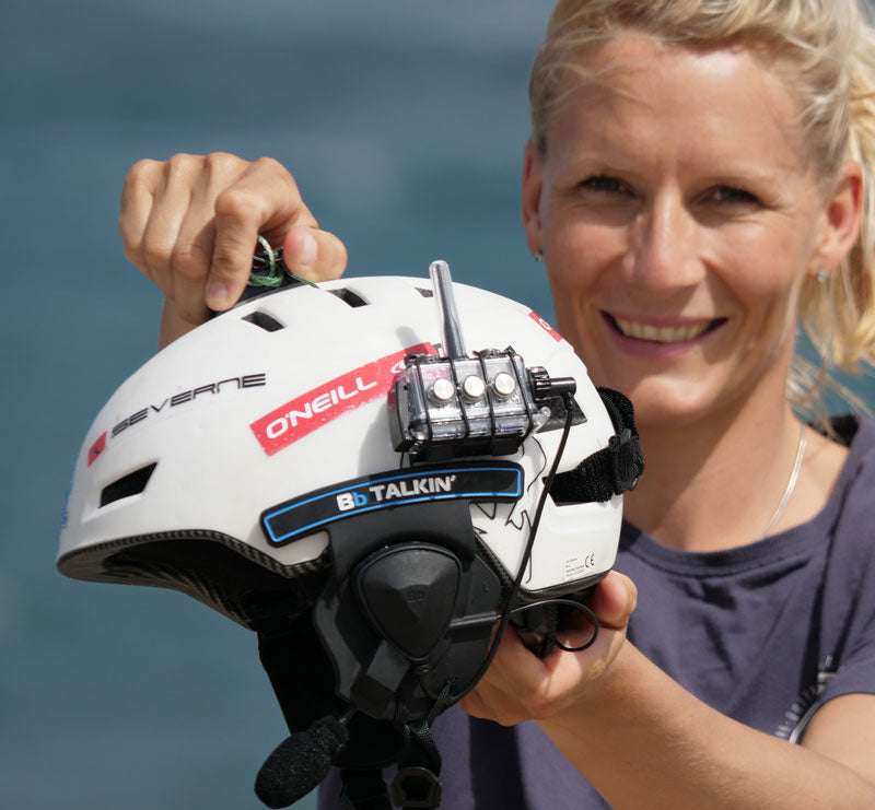 Watersports instructor demonstrating BbTalkin intercom mounted on white helmet by the water