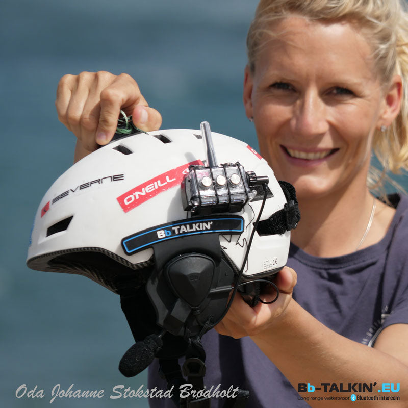 Person holding a white helmet with communication device against a blue water background
