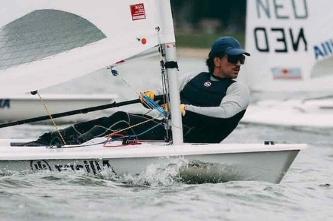 Olympic sailor Francisco Guaragna sailing on a small boat on rough ocean wearing a blue hat and sunglasses