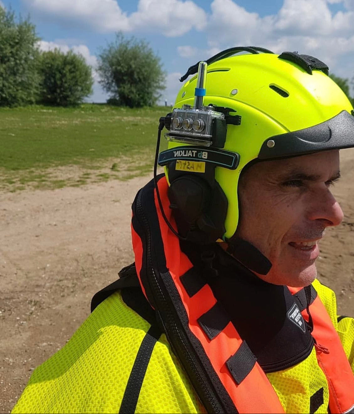 Rescue worker wearing a high-visibility helmet with Bbtalkin device and jacket outdoors on a sunny day.