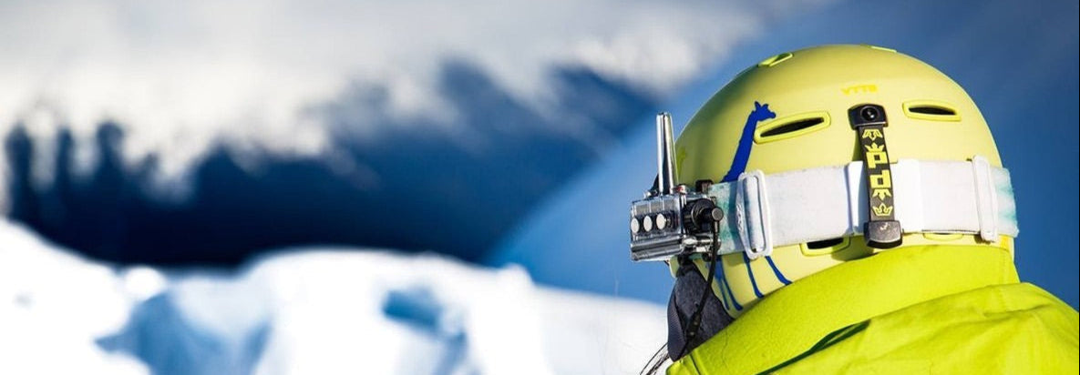 Person in a bright yellow helmet and BbTalkin device, and jacket with a blue backpack against a snowy mountain background