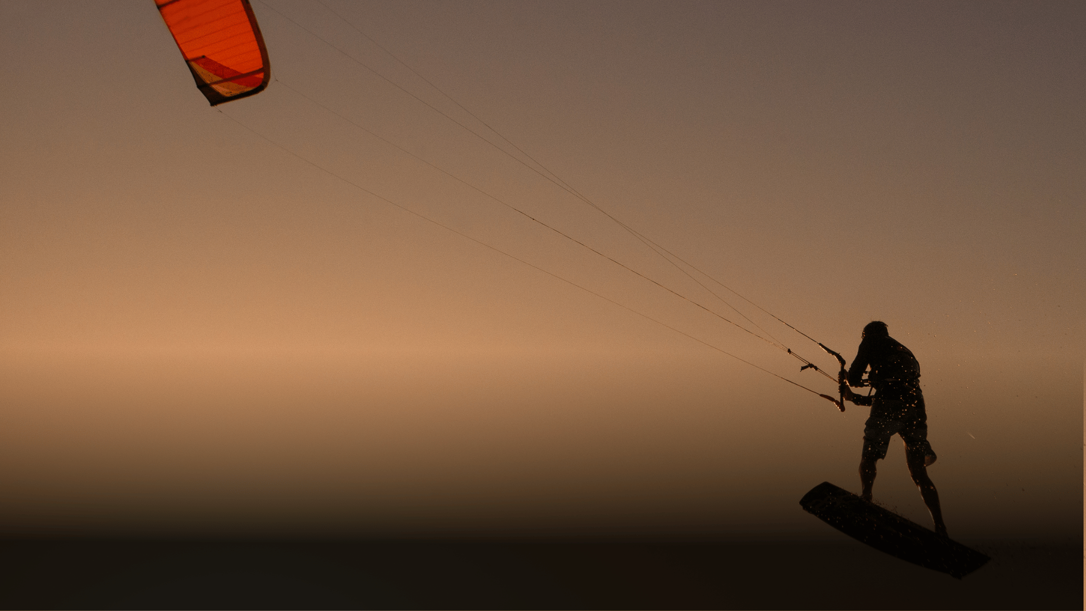 Person kite surfing at sunset with an orange kite.