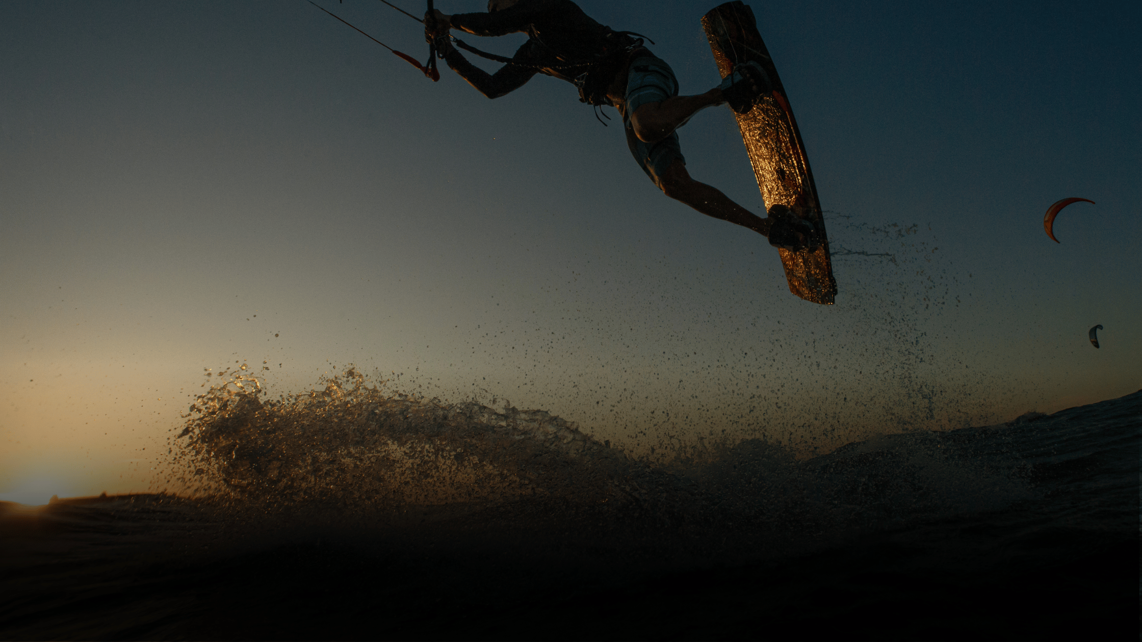 Person kiteboarding in mid-air with a sunset or sunrise background