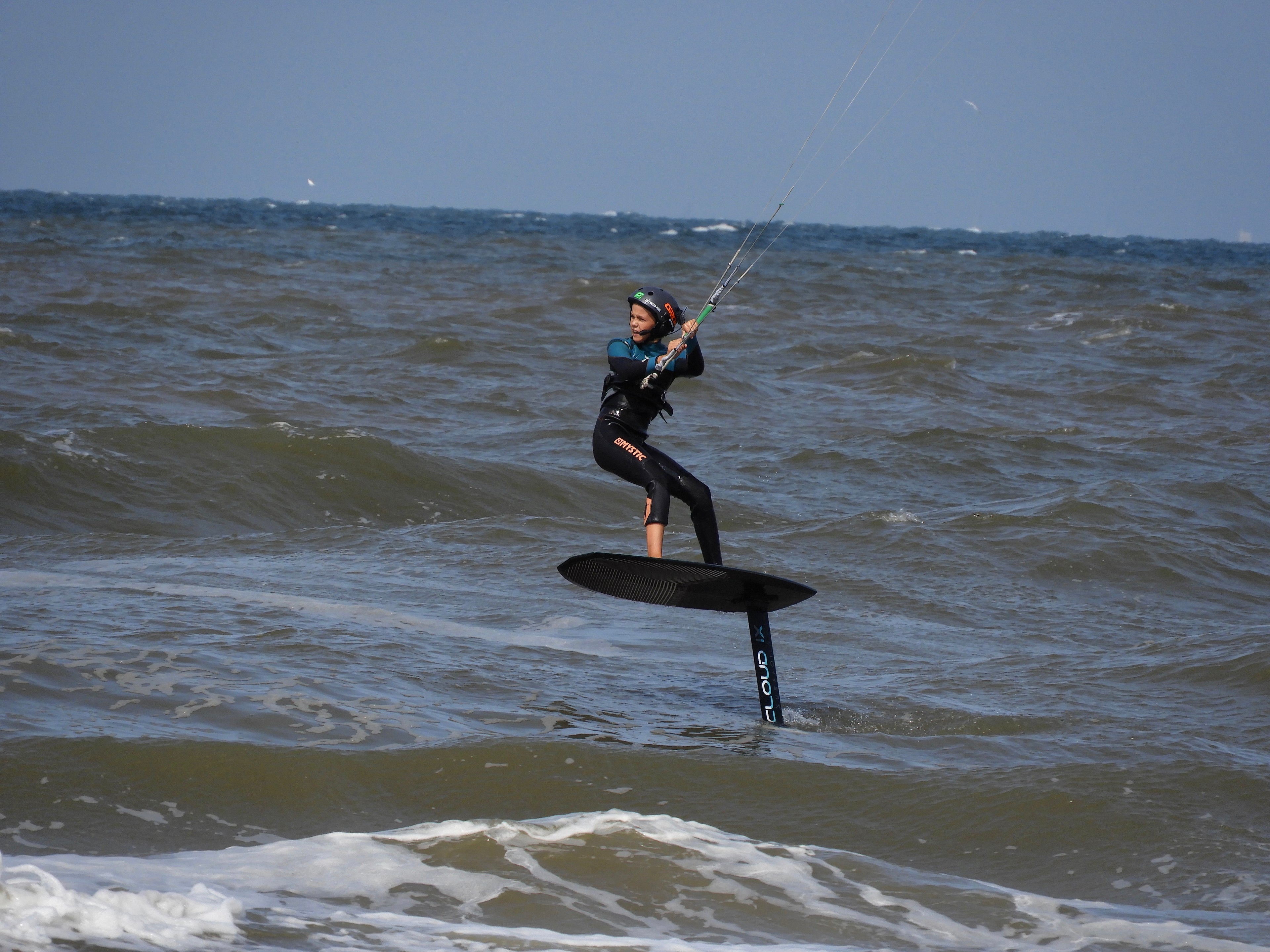 Kitefoiler riding above choppy ocean water using a hydrofoil board, showing a typical watersports environment for long-range waterproof communication systems.