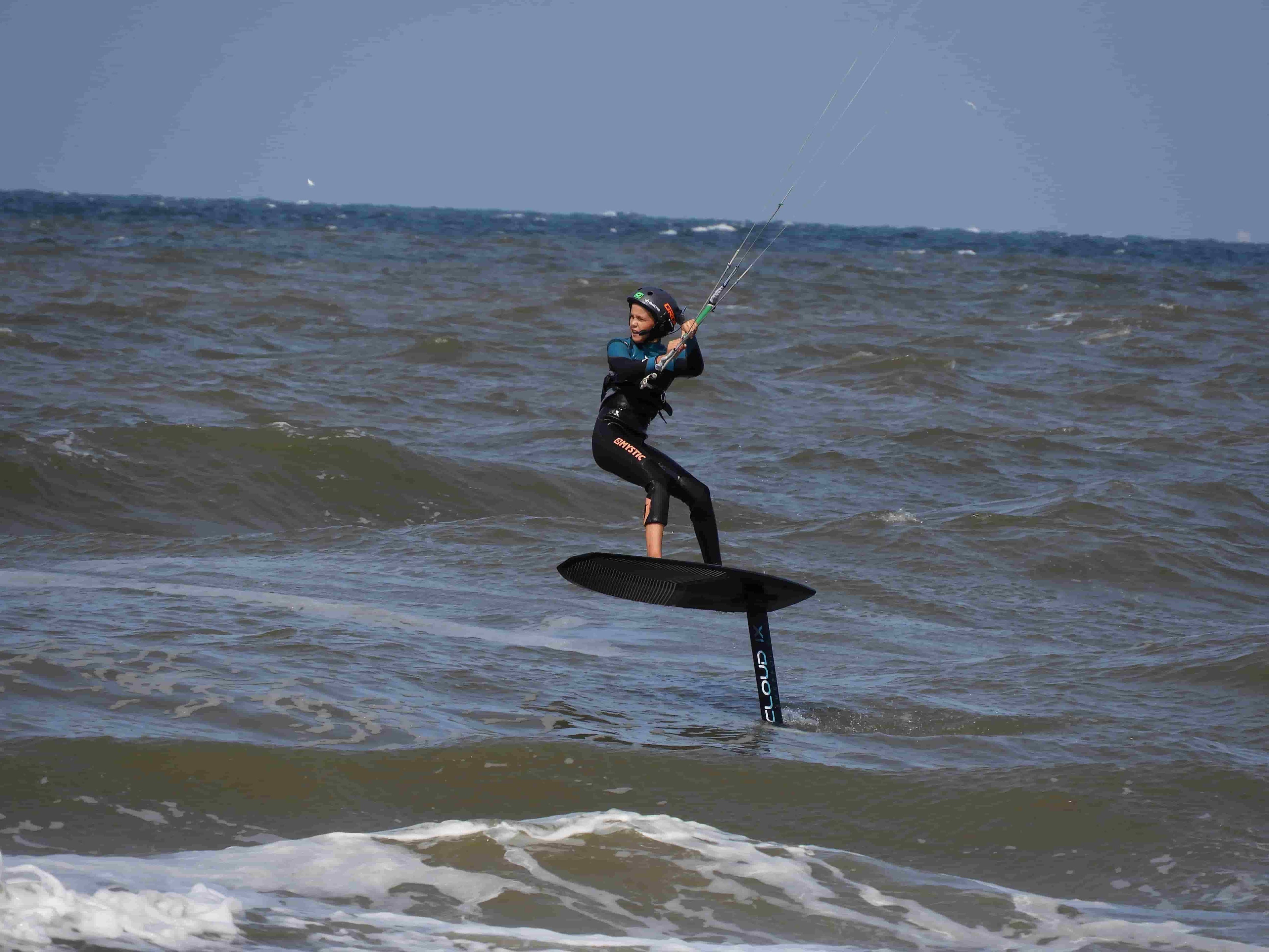 a young boy wingfoiling, wearing a helmet and bbtalkin headset on rough sea water