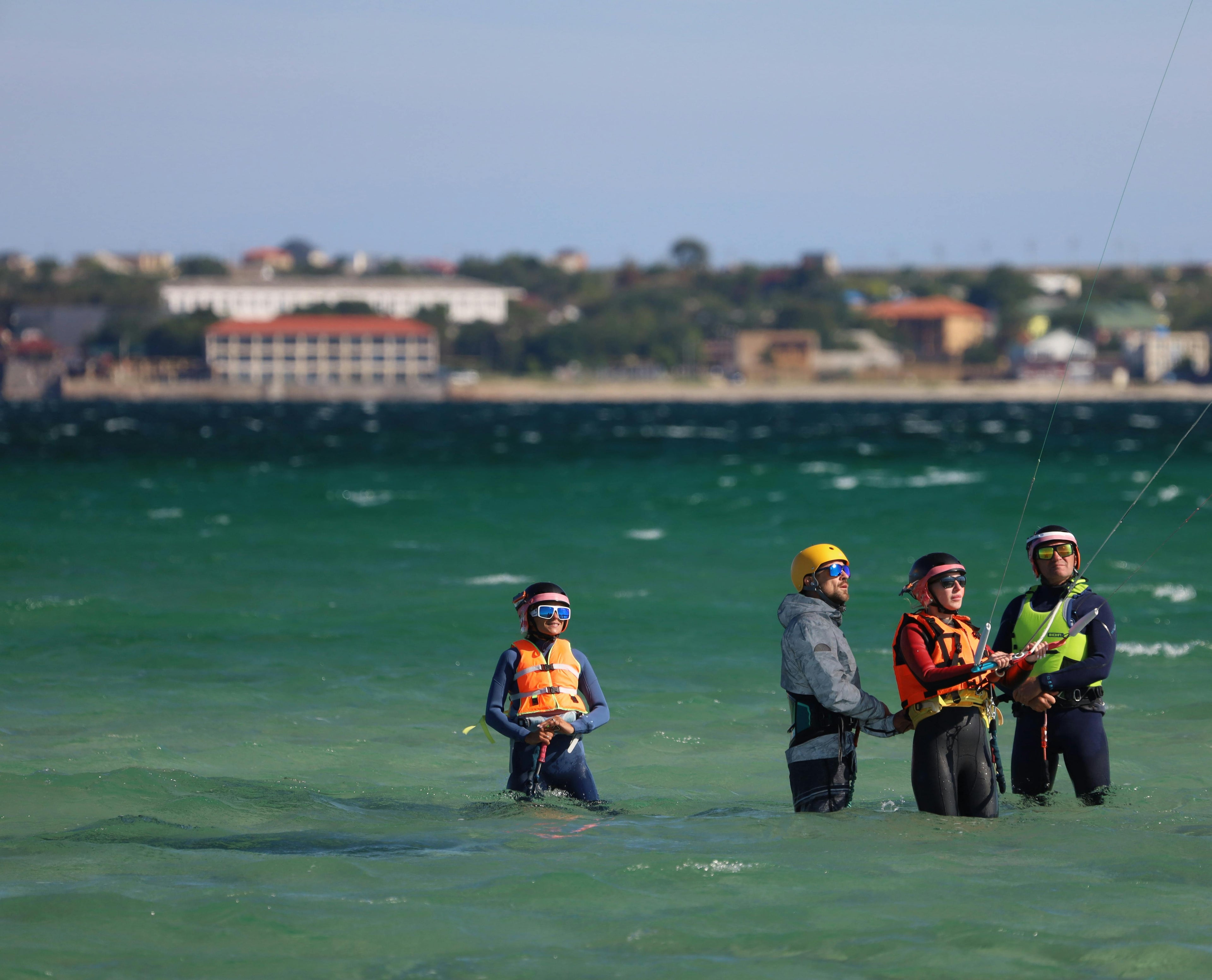 Group of kitesurf students and an instructor standing in shallow water during a lesson, showing a typical water-sports coaching setup.
