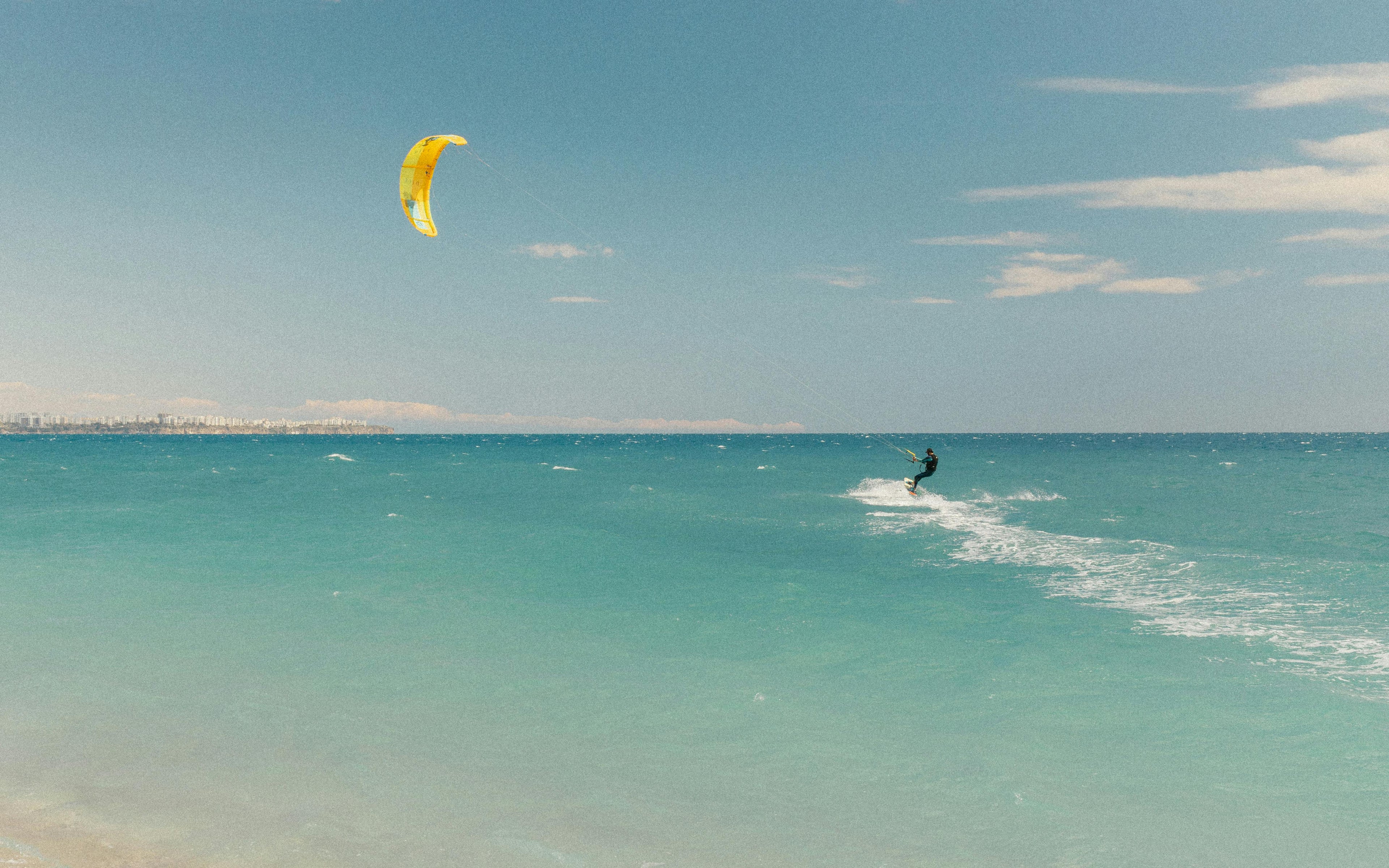 Kitesurfer riding over clear blue water with a yellow kite, showing a typical environment for water-sports communication systems.