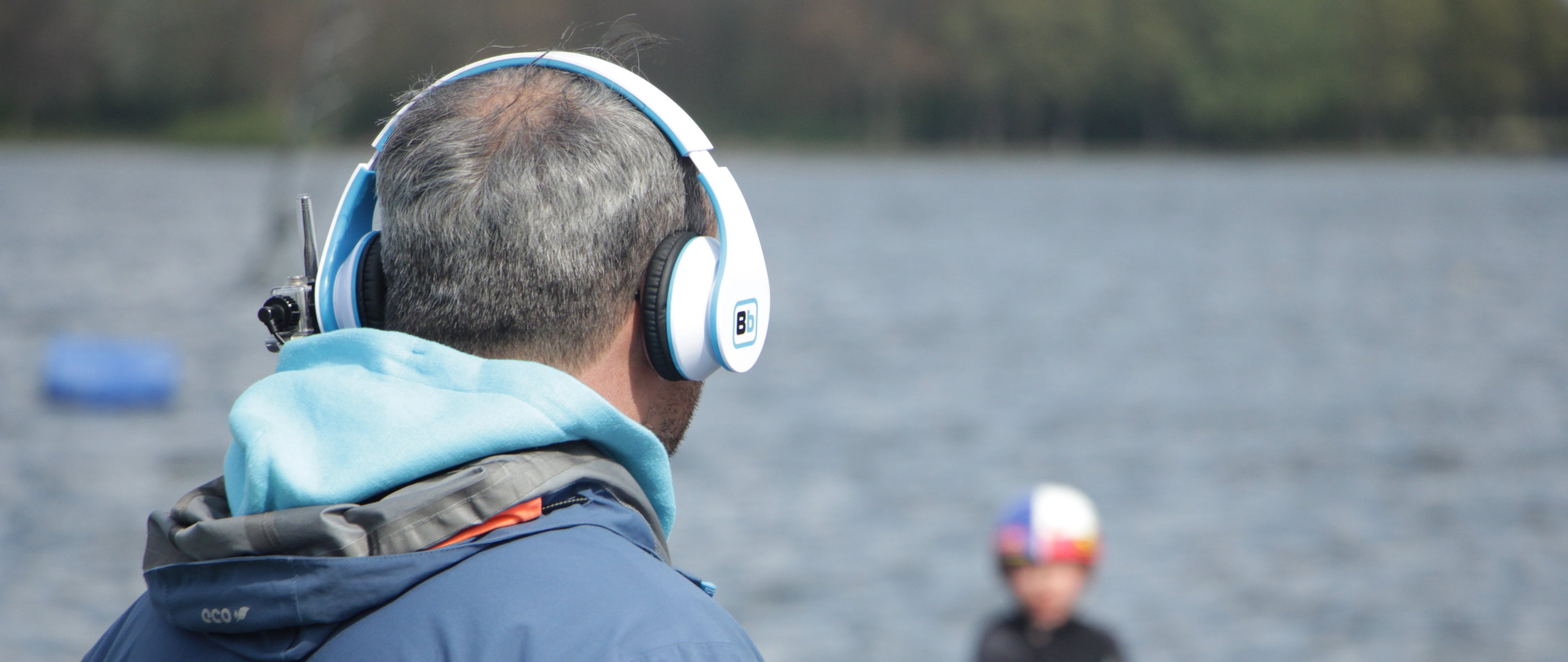 Instructor wearing a BbTalkin stereo headset by the water while coaching a rider, showing hands-free communication for watersports.