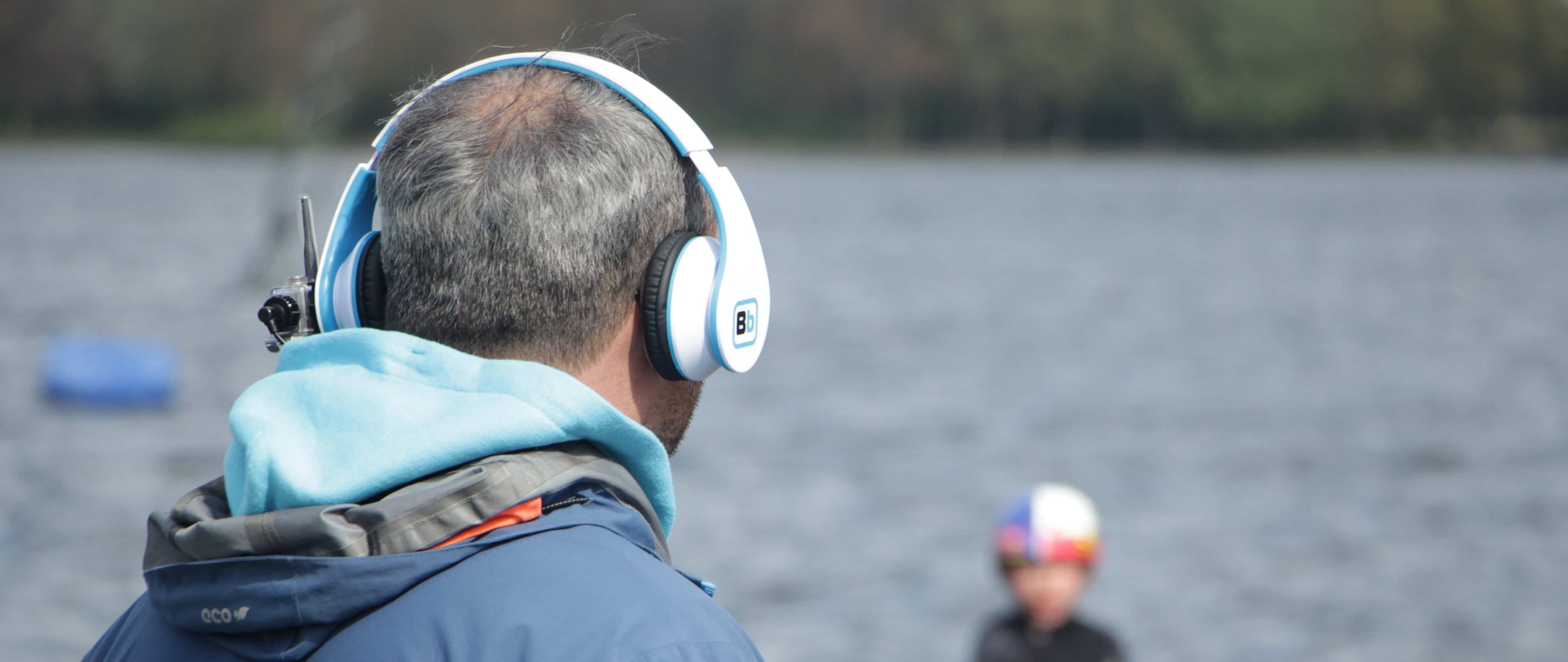 Instructor wearing a BbTalkin stereo headset by the water while coaching a rider, showing hands-free communication for watersports.
