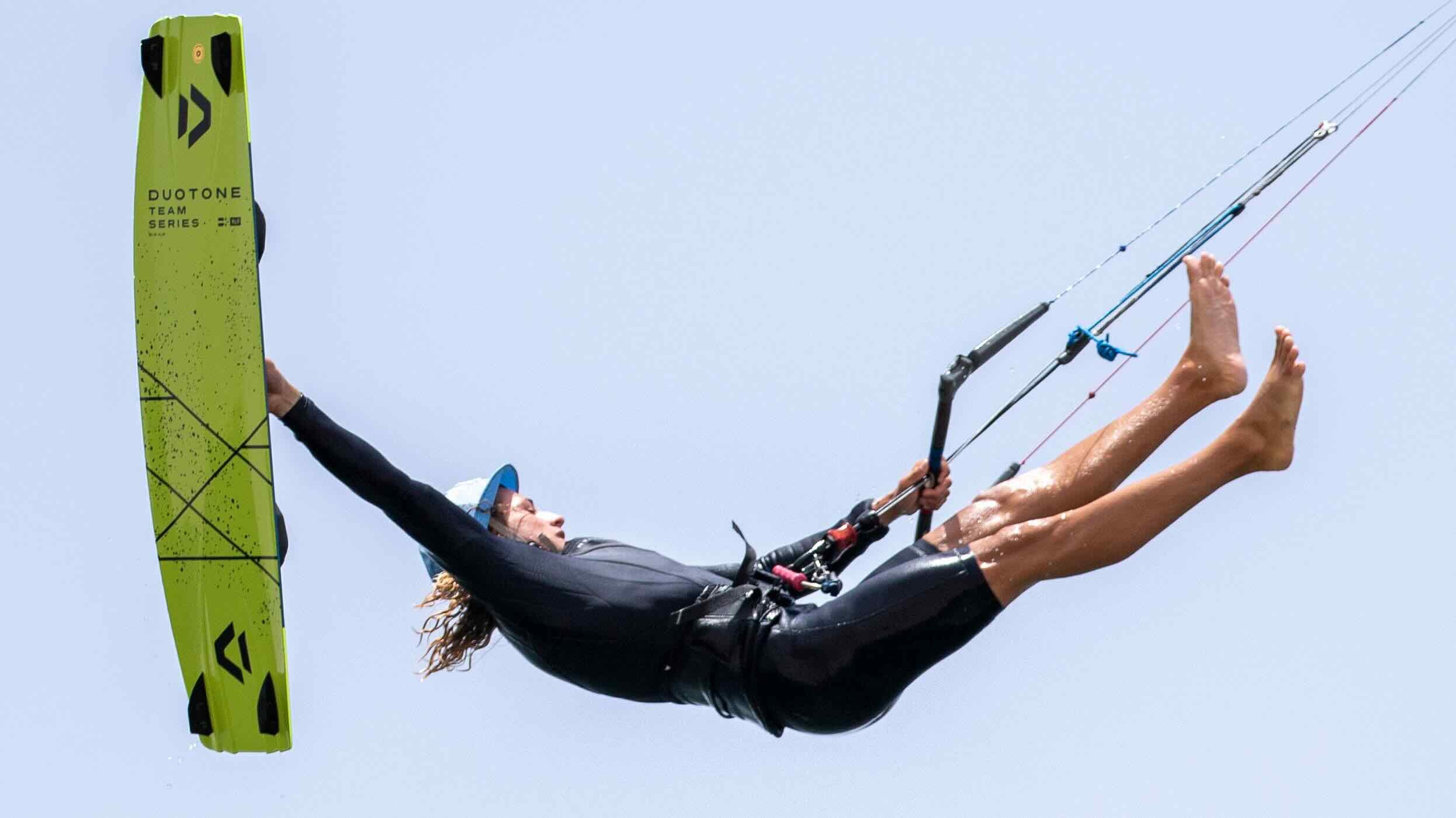 Jamie Overbeek kiteboarding with a Duotone kite in the foreground against a clear blue sky.