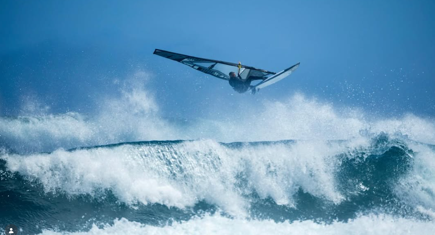 Surfboard in the air above a large wave with a clear blue sky.