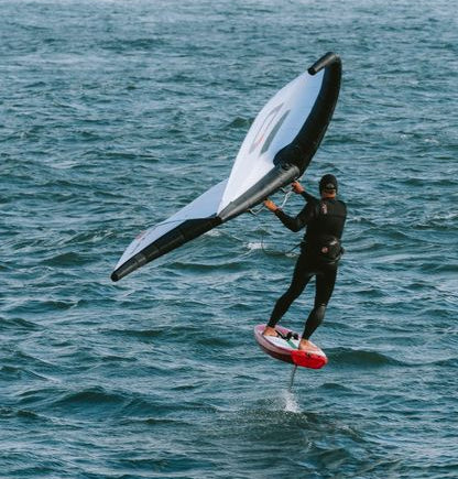 Person windsurfing on a body of water with buildings in the background