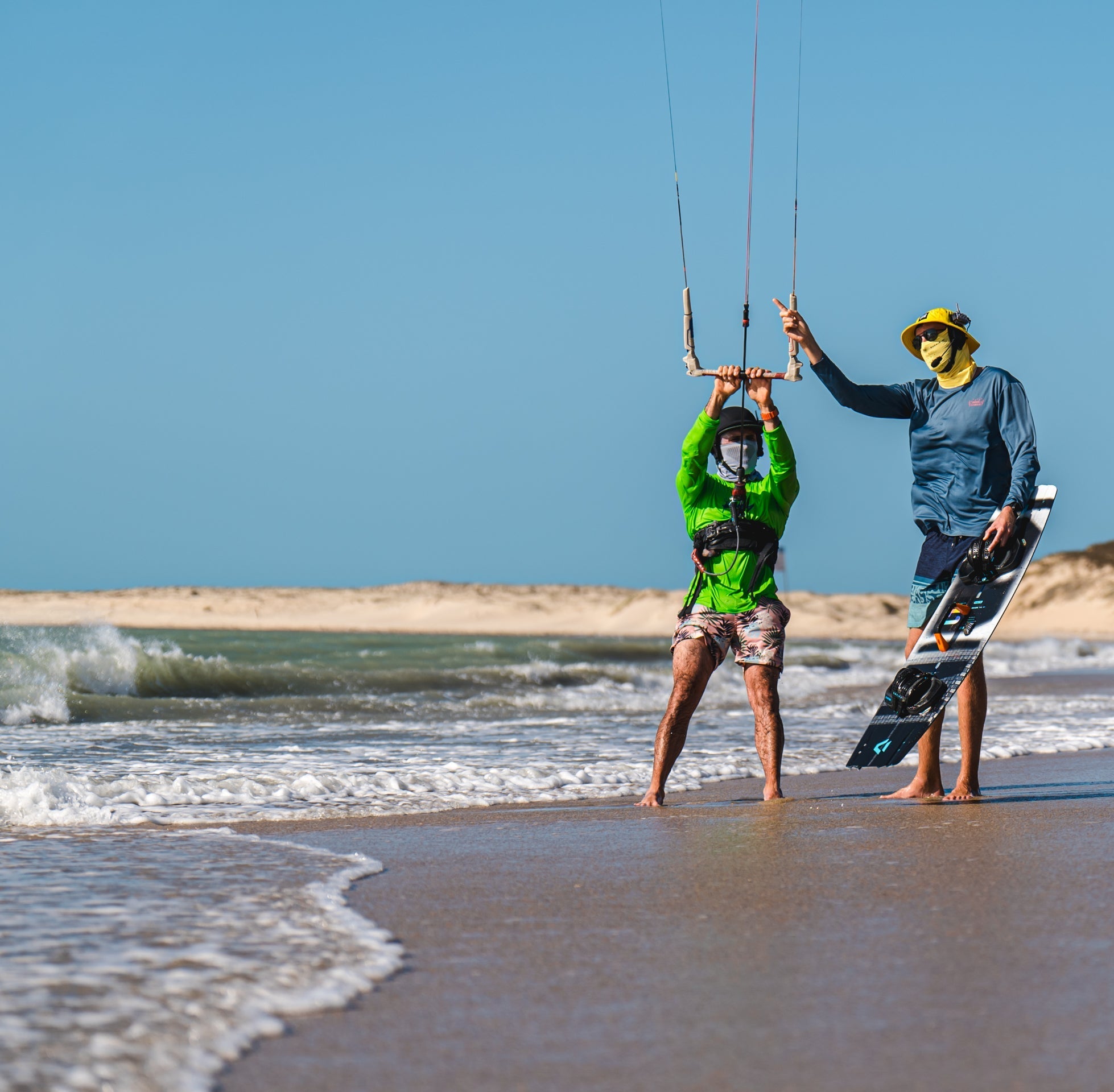 Instruktor kitesurfingu vede studenta na pláži během tréninku a ukazuje typické prostředí pro komunikační systémy pro vodní sporty.