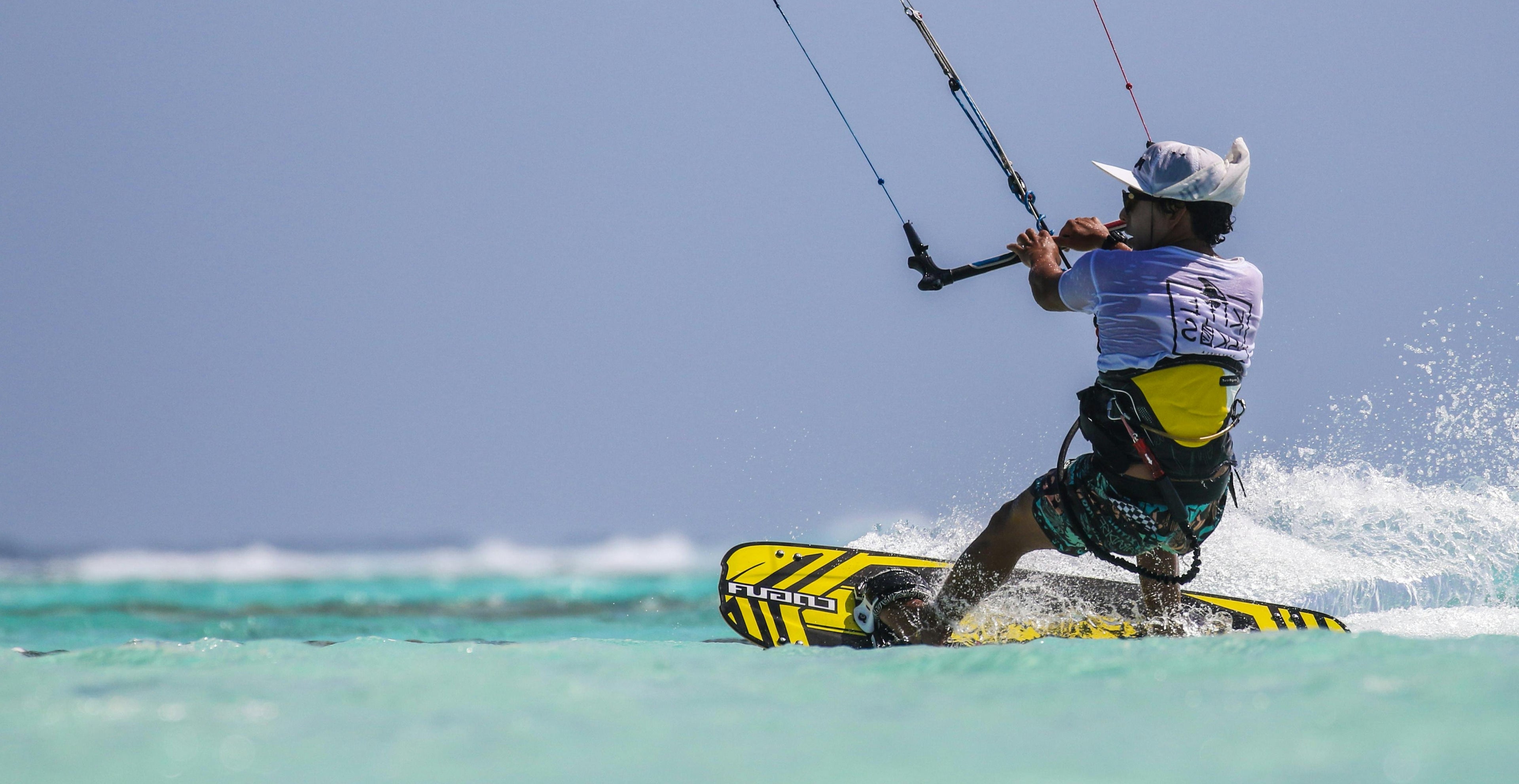 Persona practicando kitesurf en un océano azul claro con un cielo azul.