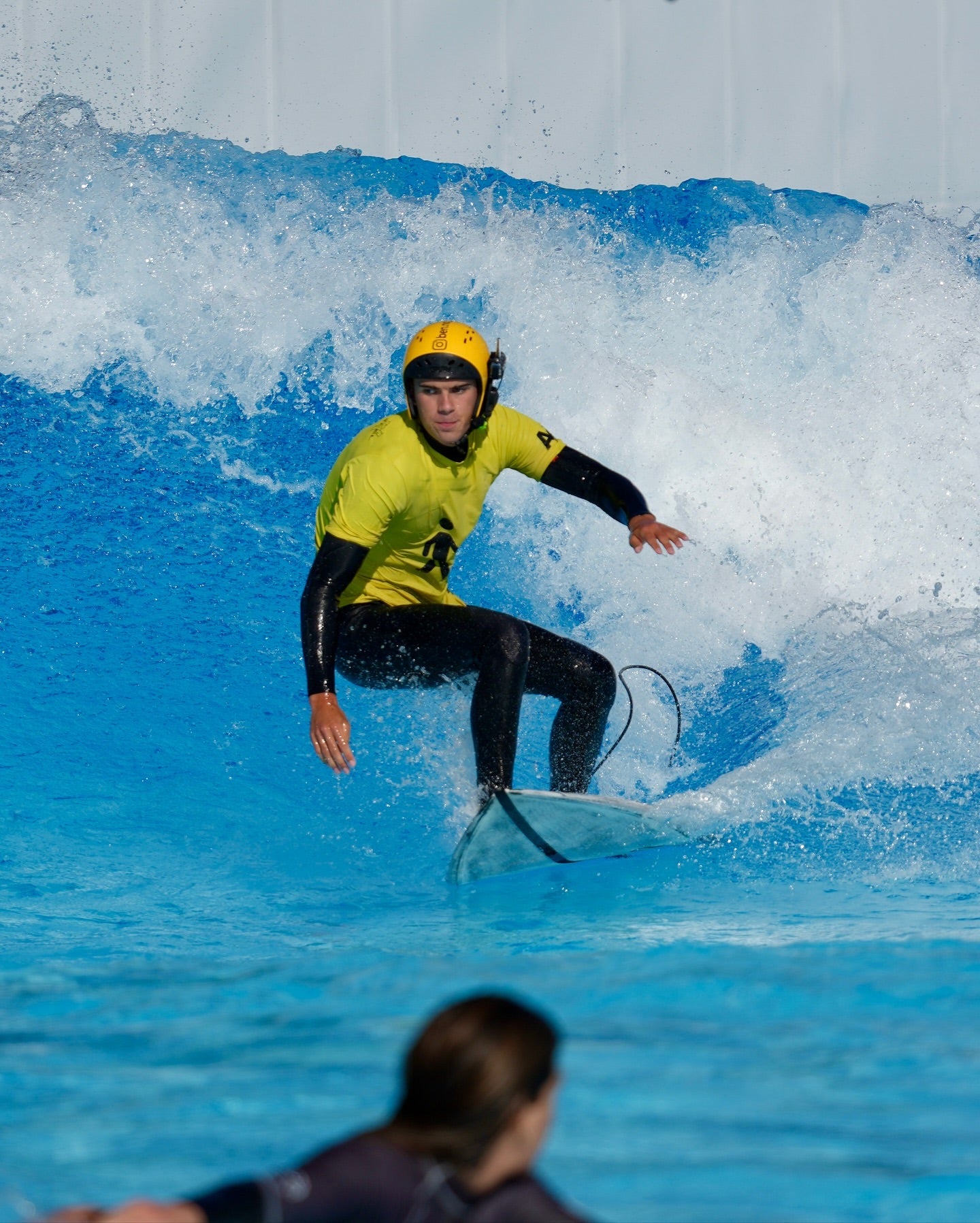 Surfista ciego con casco y auriculares BbTalkin durante un entrenamiento de surf asistido.