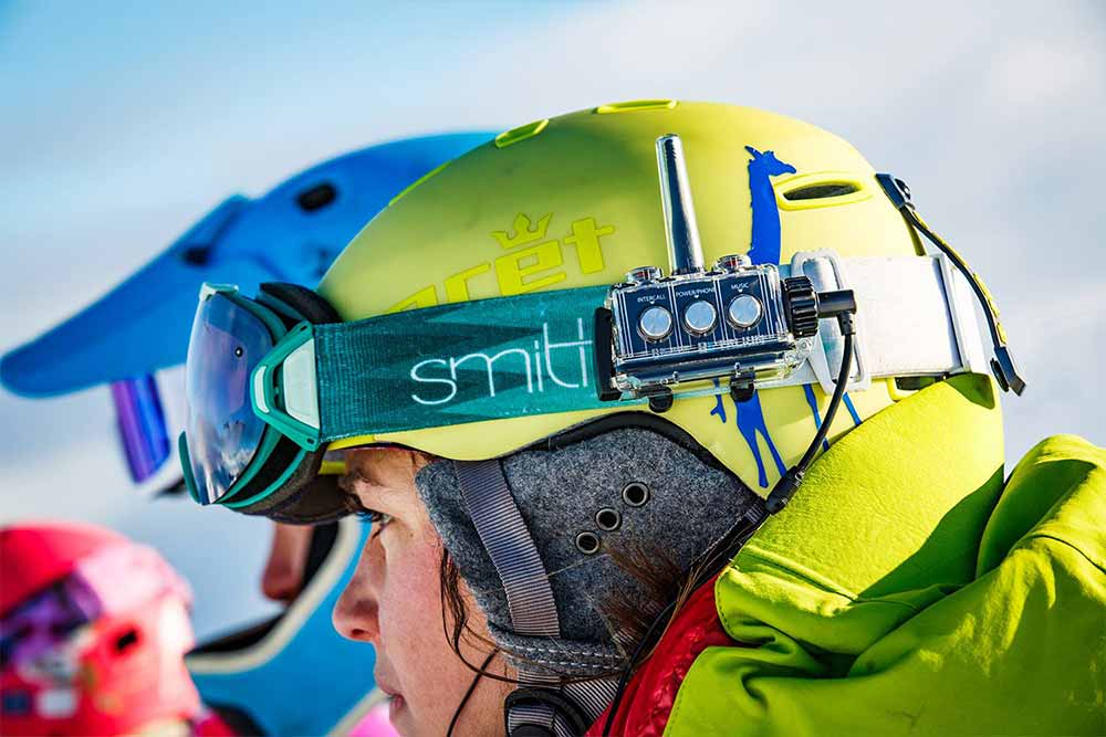 Atleta di sport invernali che indossa un casco colorato con sistema di interfono BbTalkin e occhiali protettivi su una pista innevata di montagna