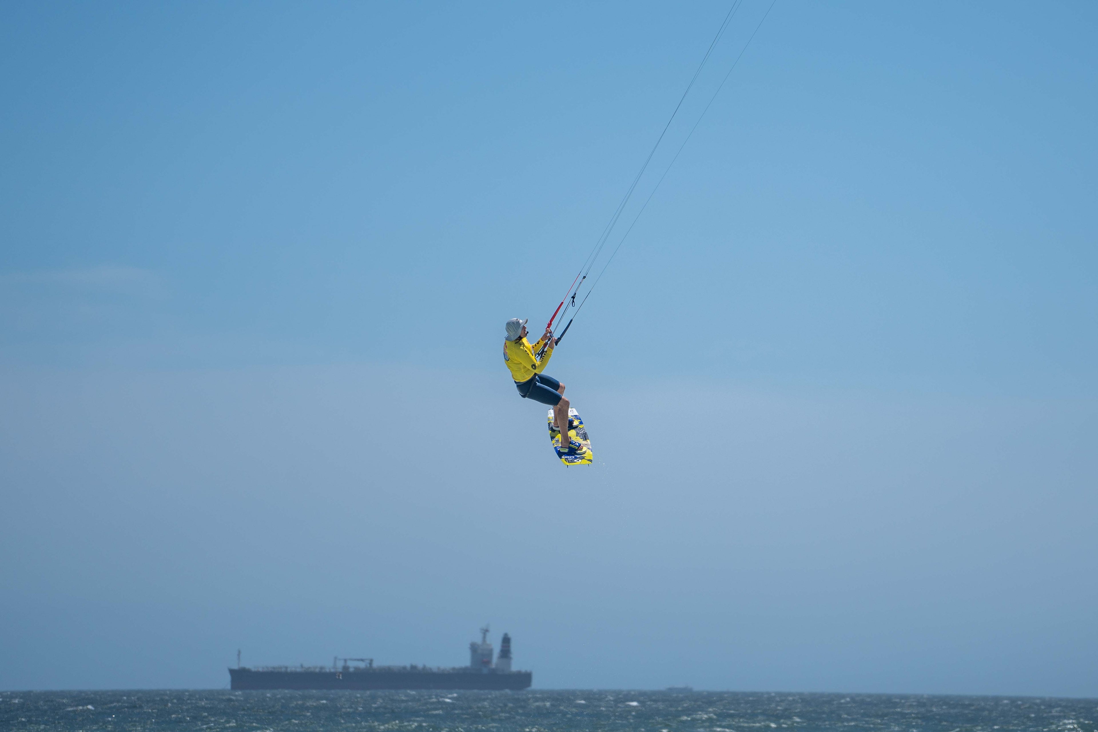 Kitesurfer che salta in alto sopra l'oceano sotto un cielo azzurro e limpido, mostrando un ambiente tipico per i sistemi di comunicazione per gli sport acquatici.