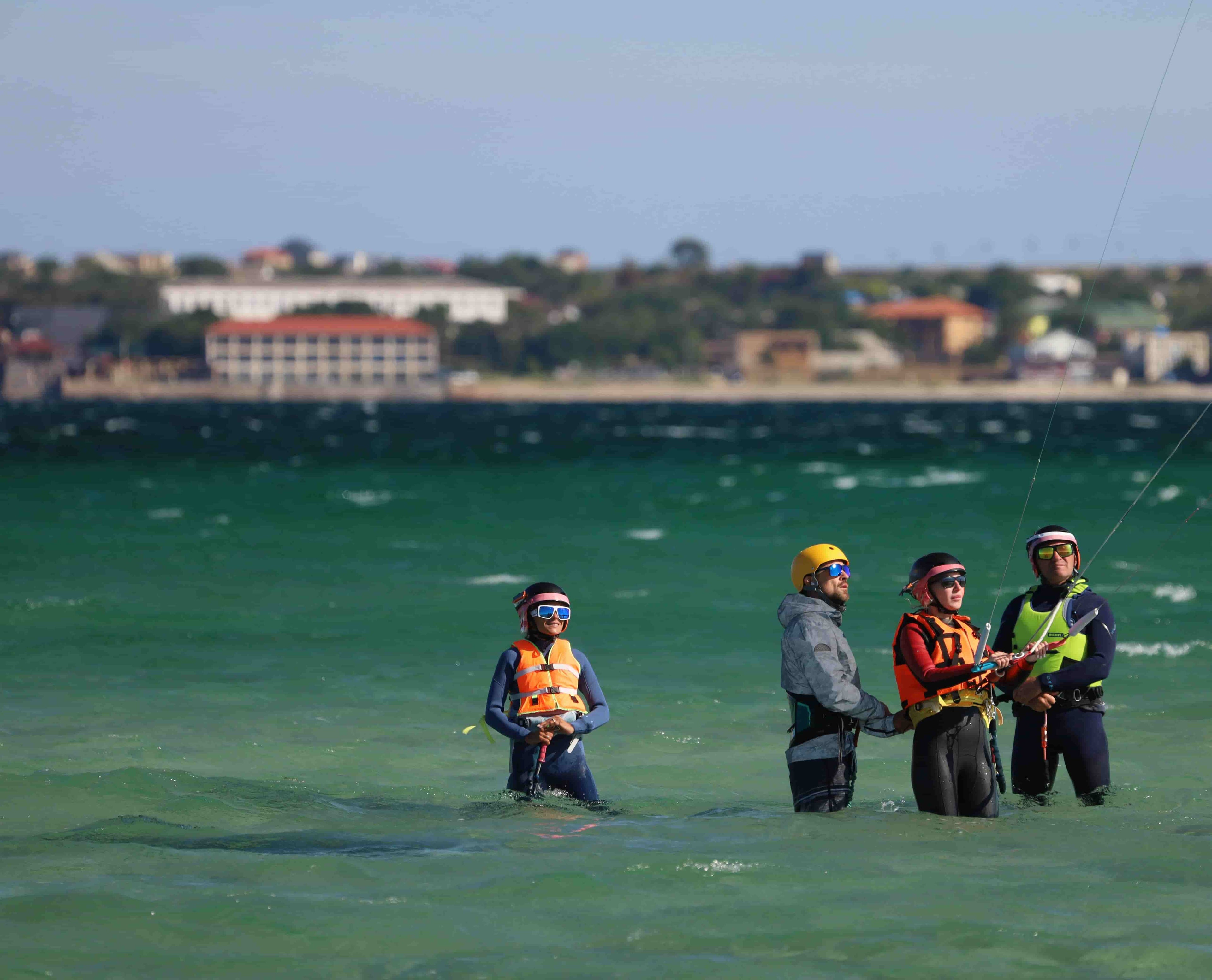 Gruppo di studenti di kitesurf e un istruttore in piedi in acque poco profonde durante una lezione, che mostra una tipica configurazione di insegnamento degli sport acquatici.