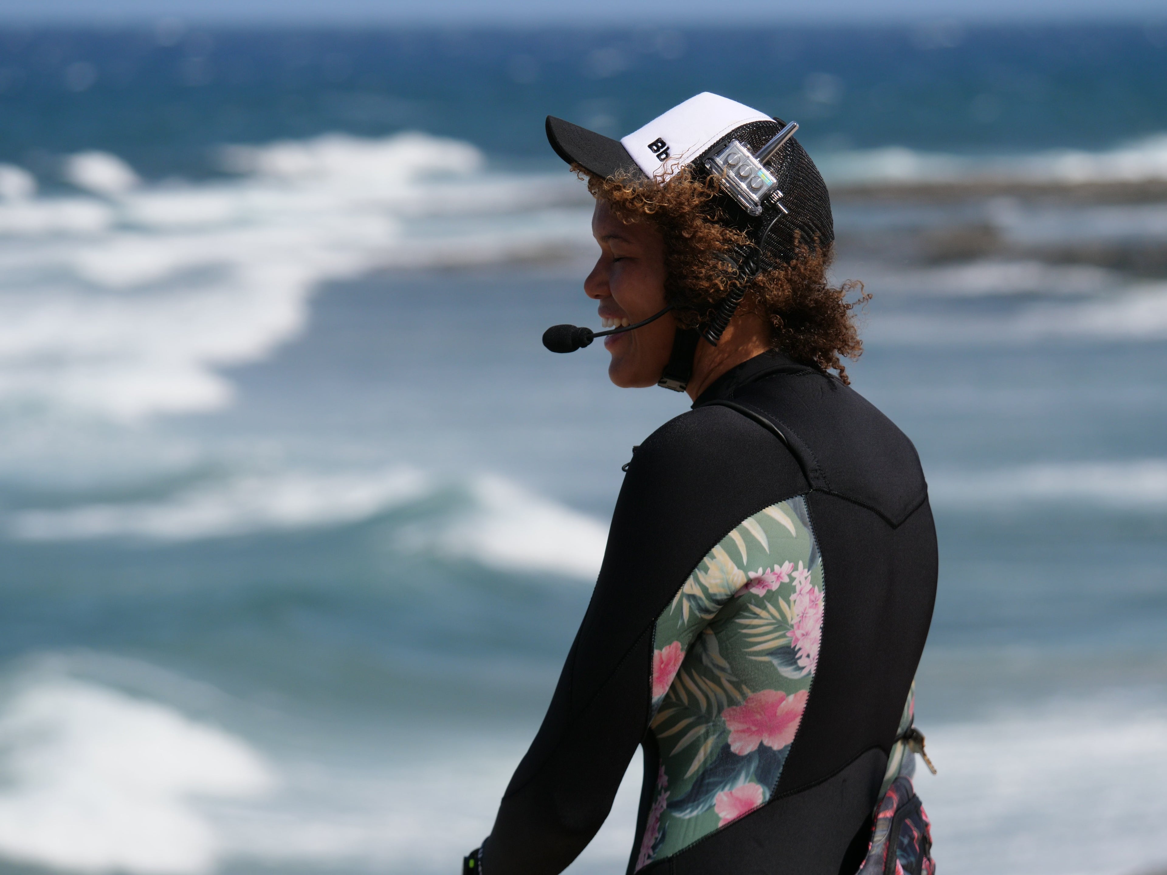 uma mulher na praia, sorrindo, usando um fone de ouvido Bbtalkin, um lindo oceano, 